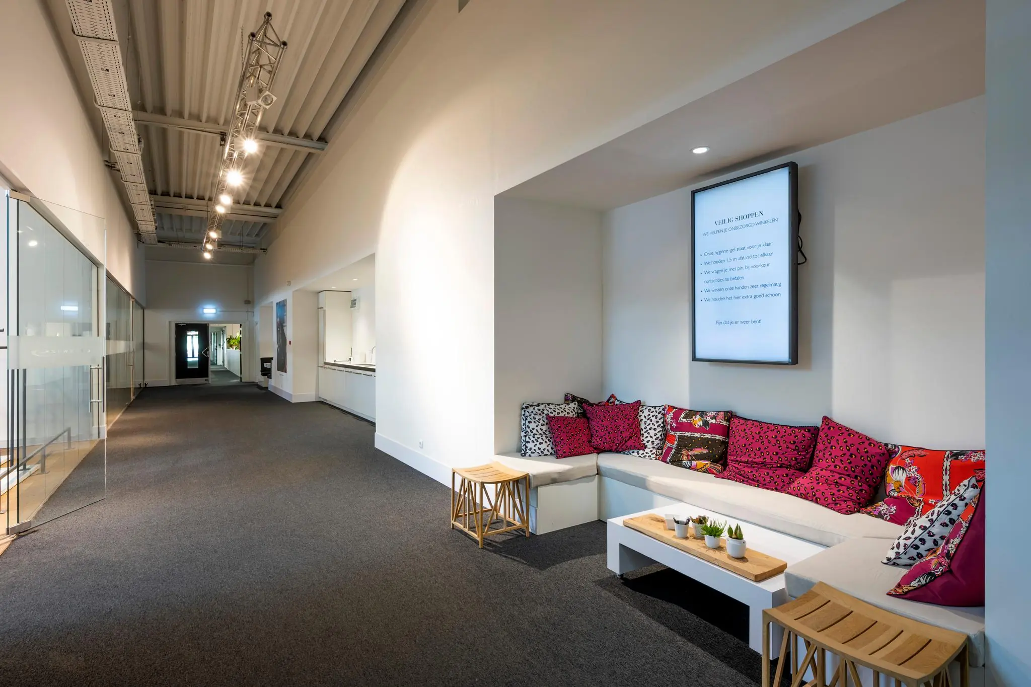 Moderne wachtruimte met een witte zithoek, kleurrijke kussens en een informatiebord aan de muur in Stammerhove.