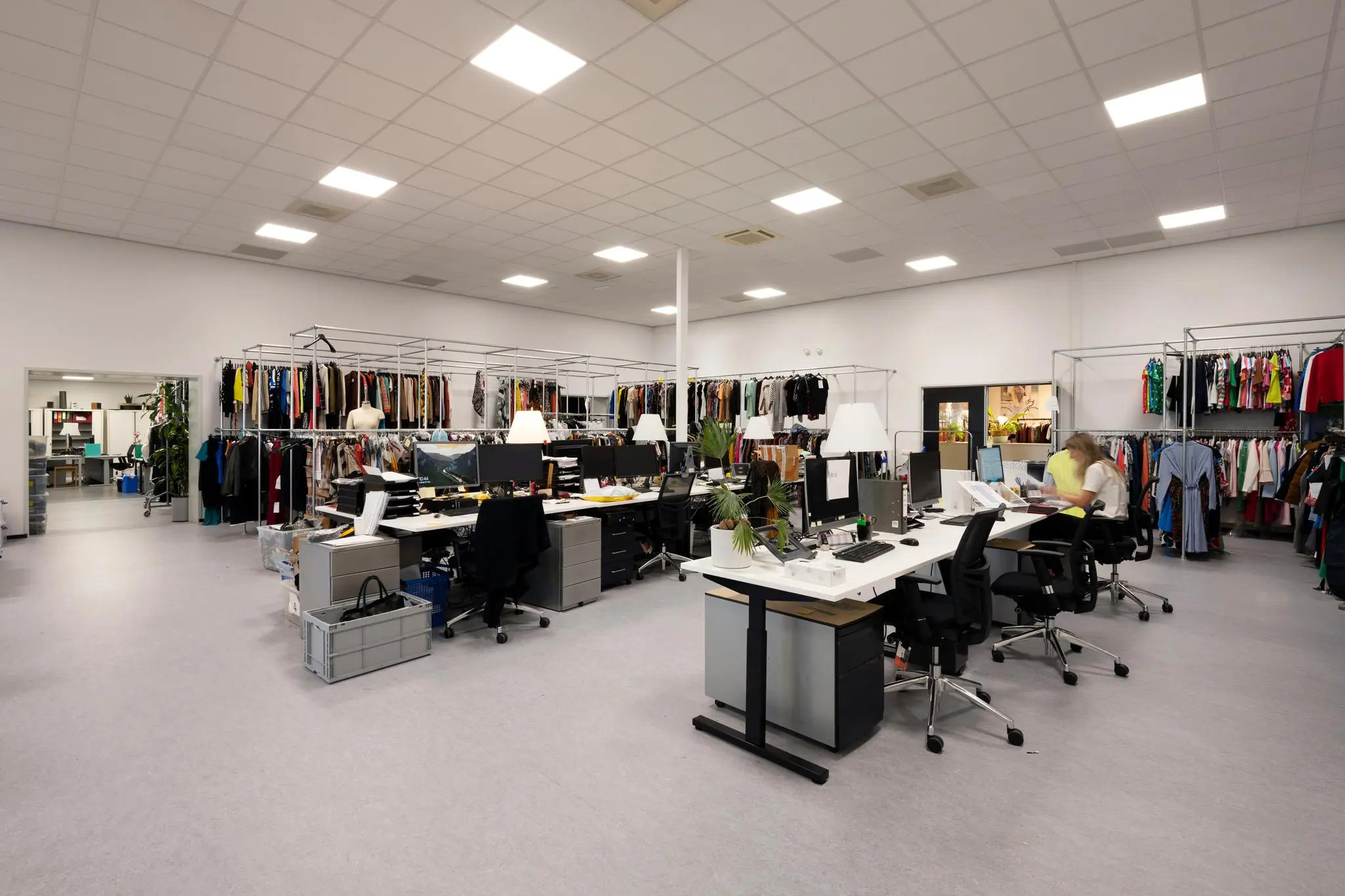 Open kantoorruimte bij Stammerhove met werkplekken en rekken vol kledingstukken.
