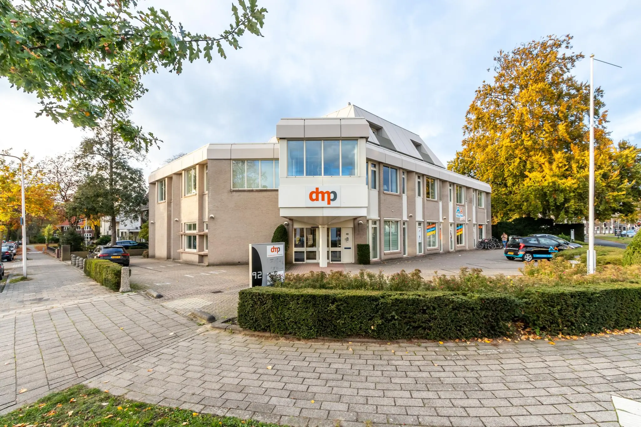 Kantoorpand van dmp aan de Utrechtseweg met parkeerplaatsen en herfstbomen op de achtergrond.