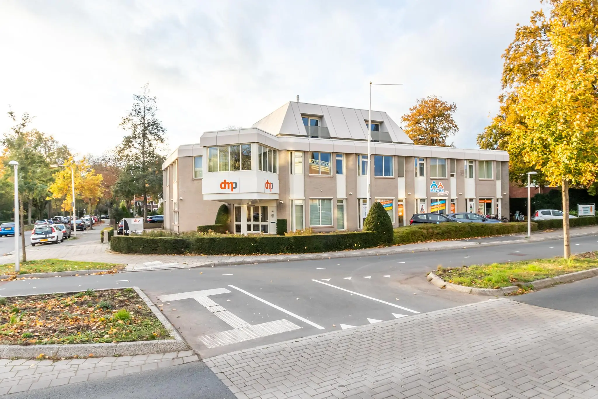 Kantoorpand aan de Utrechtseweg met bedrijfslogo’s van dmp en Maklam, gelegen op een hoek met een rotonde en omgeven door herfstkleurige bomen.