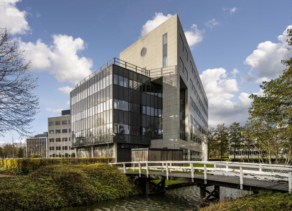 Modern kantoorgebouw aan de Neptunusstraat met glazen gevel en wit bruggetje over het water op de voorgrond.