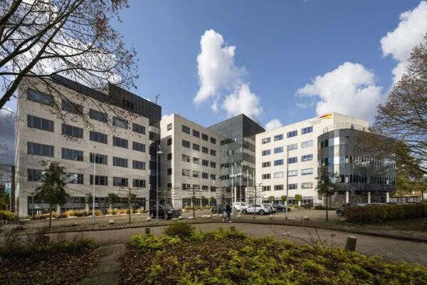 Kantoorgebouw aan de Neptunusstraat met moderne gevel en omliggende parkeerplaats, gefotografeerd op een zonnige dag.