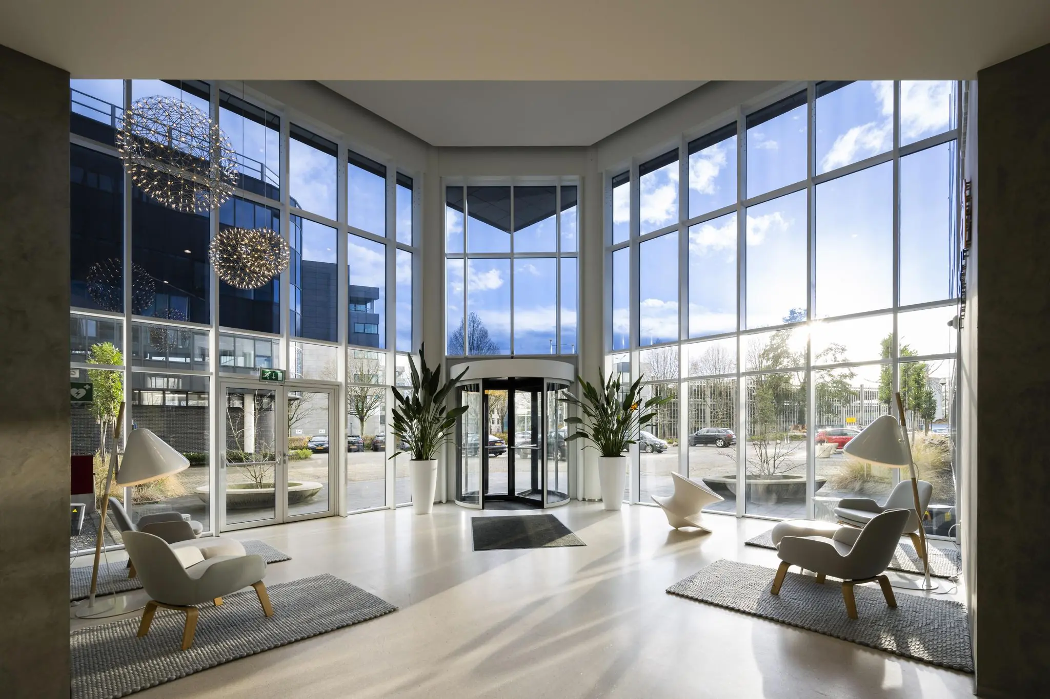 Moderne en lichte entreehal aan de Neptunusstraat met grote glazen gevel, designmeubels en planten.