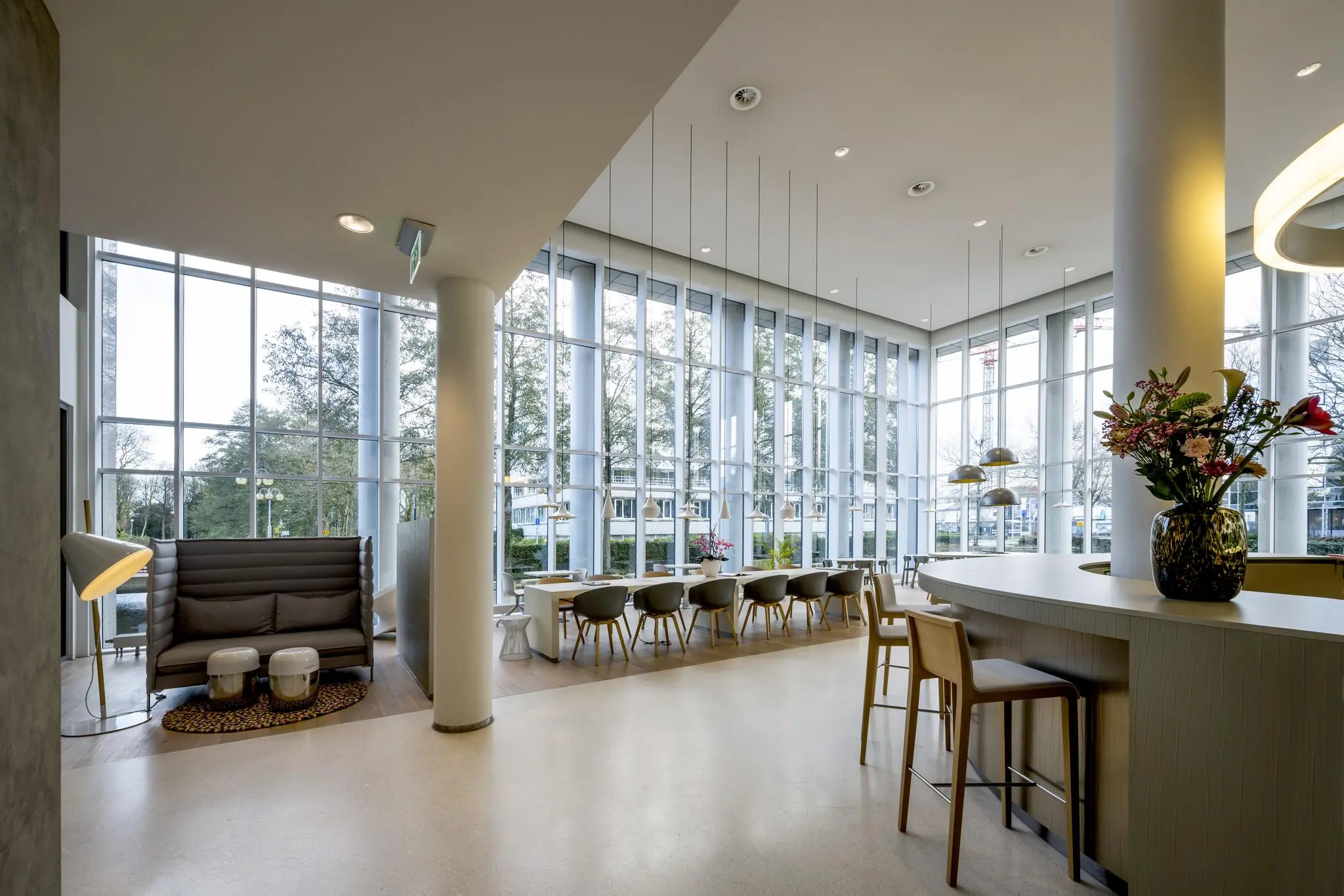 Moderne, lichte kantoorlobby aan de Neptunusstraat met hoge ramen, zitplekken en een bloemetje op de balie.