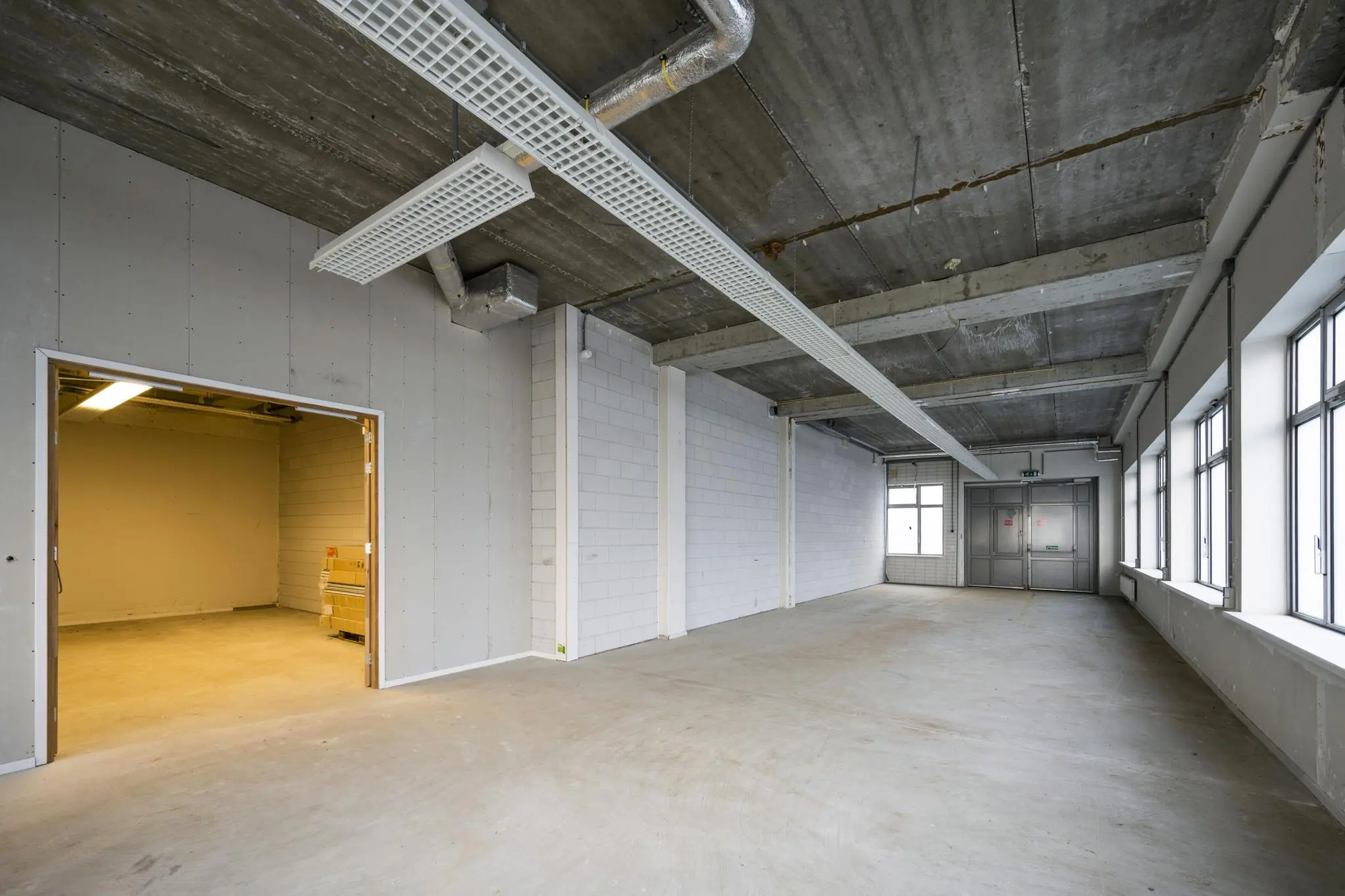 Leeg industrieel bedrijfs- of kantoorruimte aan de Neptunusstraat met betonnen vloer, systeemplafond en grote ramen.