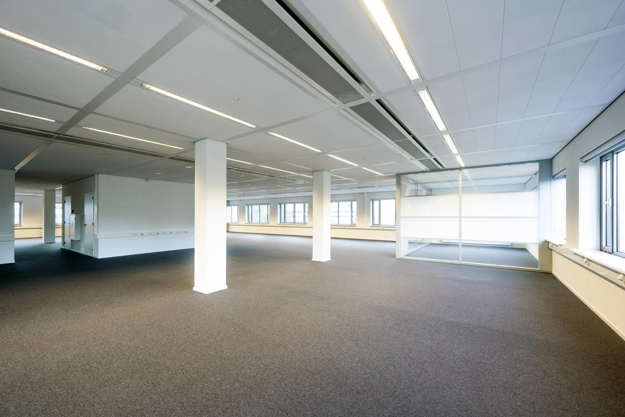 Licht en ruim leeg kantoorpand aan de Neptunusstraat met tapijtvloer, systeemplafond en glazen vergaderruimte.