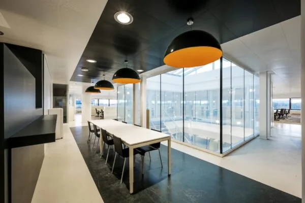 Moderne kantoorruimte aan de Prof. E.M. Meijerslaan met een lange vergadertafel, grote zwarte lampen en glazen wanden rond een atrium.