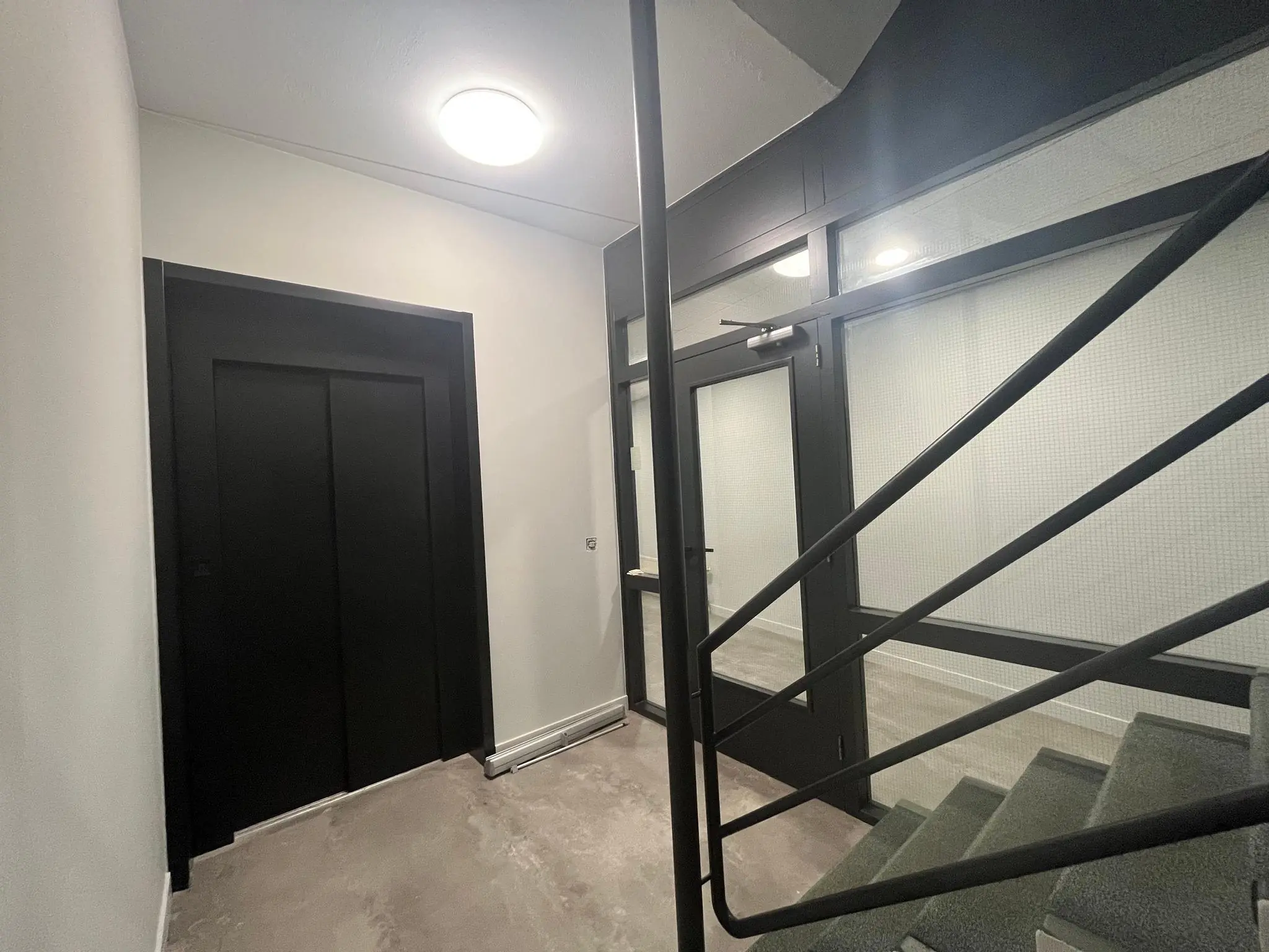 Ingang van een modern trappenhuis met een zwarte liftdeur en glazen toegangsdeur aan de Koningsweg.