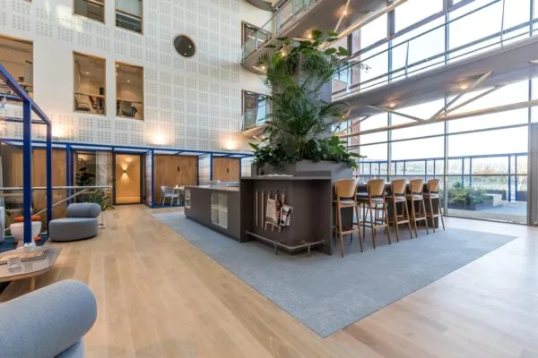 Moderne, lichte kantoorlobby aan de Kabelweg met zitgedeelte, hoge plantenbak en bar met barkrukken.
