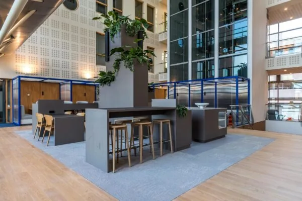 Moderne kantoorruimte aan de Kabelweg met hoge plafonds, glazen wanden, planten en zitgelegenheden.