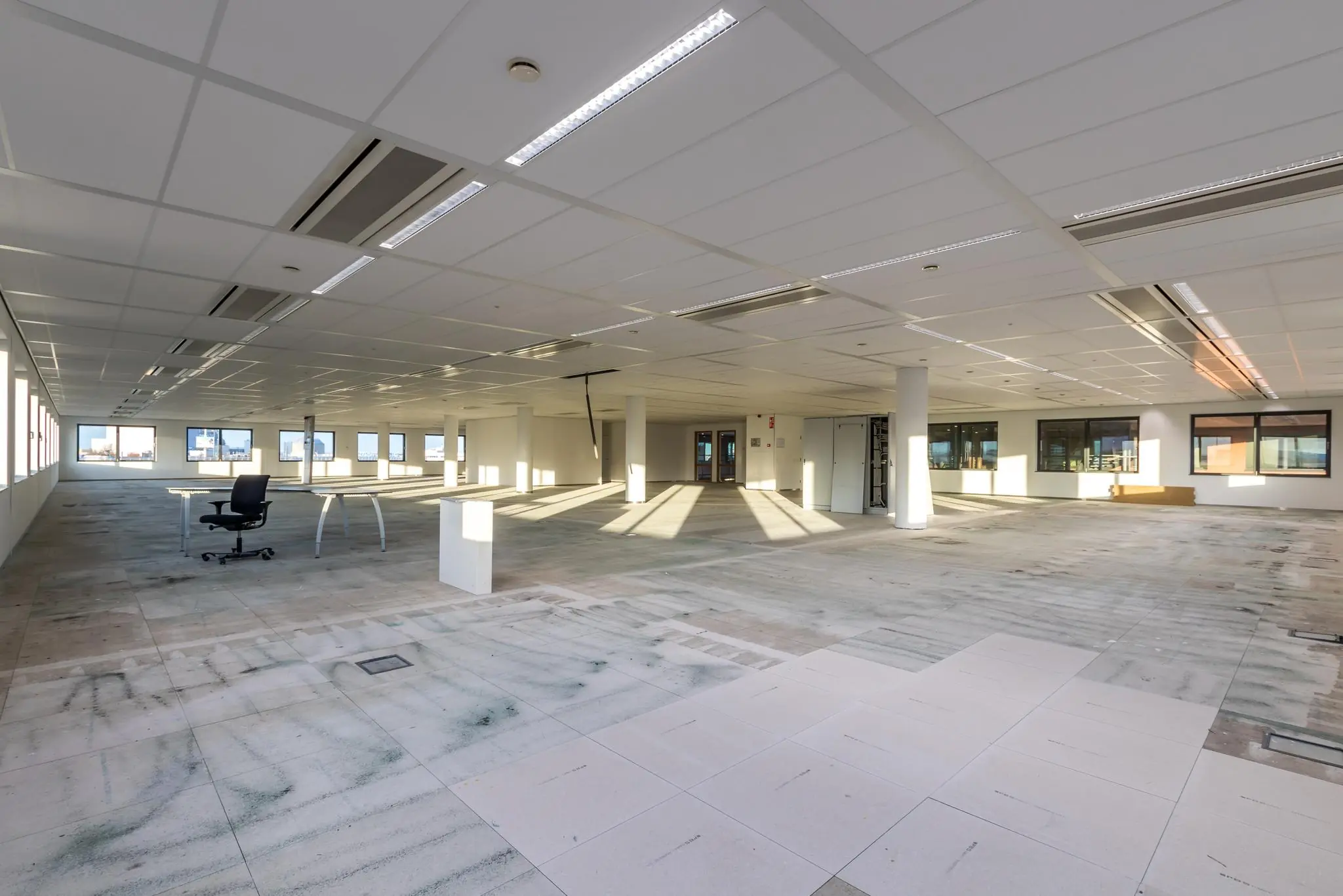 Leeg kantoorpand aan de Kabelweg met systeemplafond, betegeldevloer en enkele losse bureaus.
