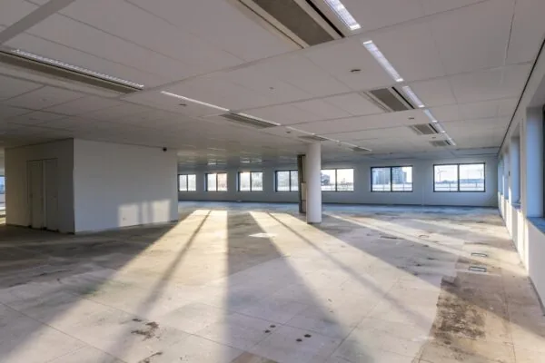 Leegstaande, zonovergoten kantoorruimte aan de Kabelweg met grote ramen en systeemplafond.