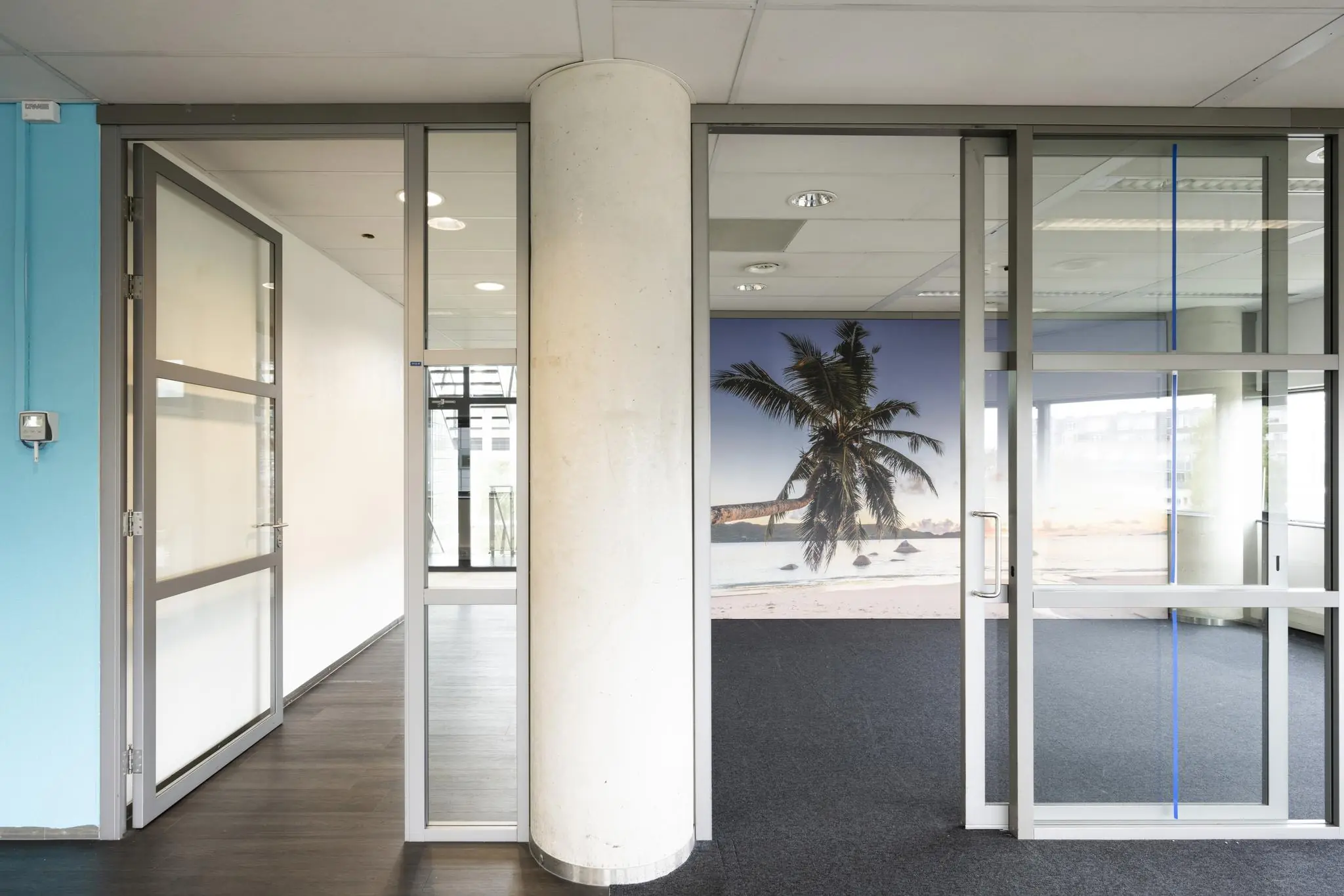 Moderne kantoorruimte in Rietlandpark met glazen wanden en een muurposter van een tropisch strand met palmboom.