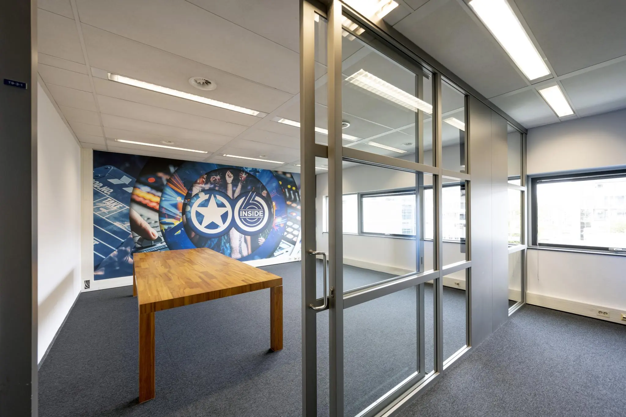 Vergaderruimte in Rietlandpark met glazen wand, houten tafel en kleurrijke muurschildering met het logo van Inside.