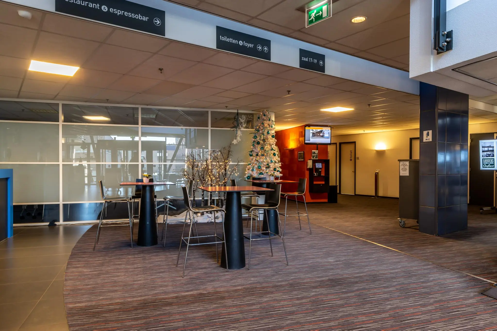 Moderne wachtruimte in gebouw aan de Oudlaan, ingericht met statafels, een witte kerstboom en sfeerverlichting.