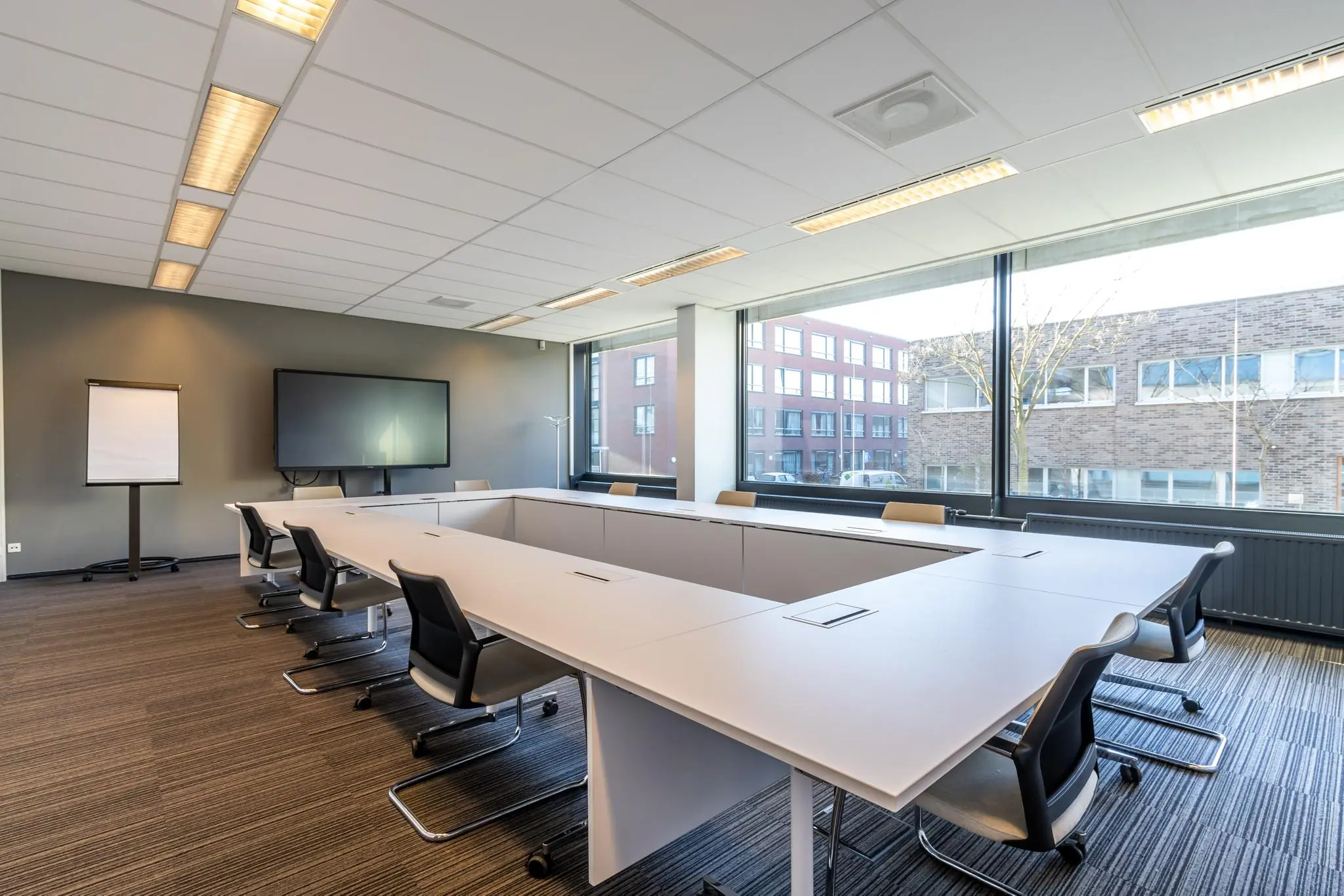 Moderne vergaderruimte aan de Oudlaan met een U-vormige tafelopstelling, grote ramen en presentatiescherm.