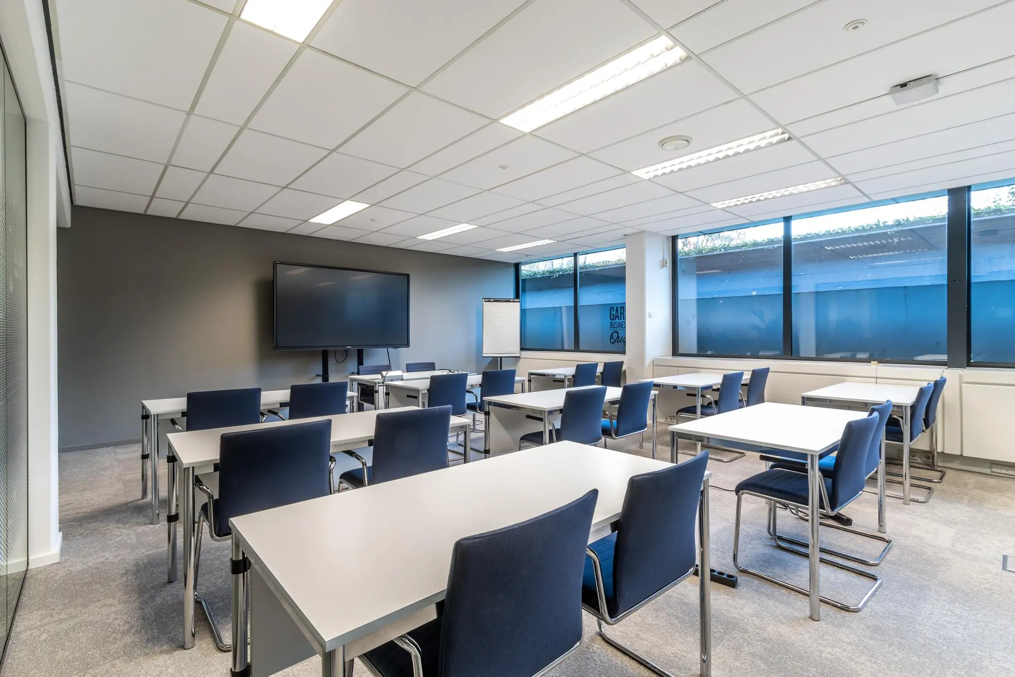 Moderne vergaderruimte aan de Oudlaan met witte tafels, blauwe stoelen, een groot presentatiescherm en natuurlijk daglicht.