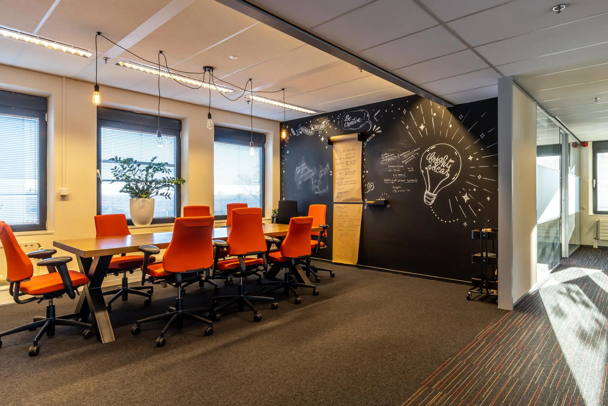Vergaderruimte aan de Oudlaan met oranje stoelen, houten tafel en een krijtbordmuur met creatieve tekeningen en notities.