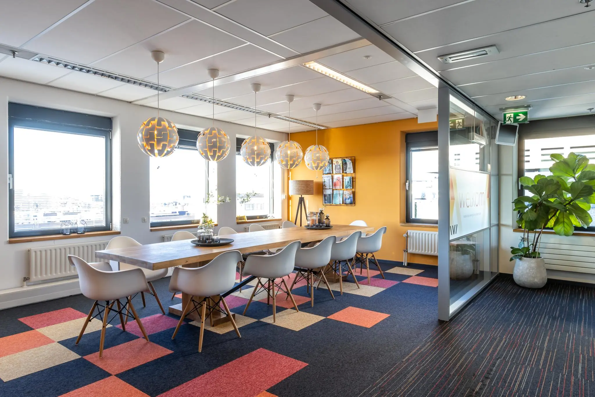 Moderne vergaderruimte aan de Oudlaan met lange houten tafel, designstoelen, kleurige vloerbedekking en grote ramen.