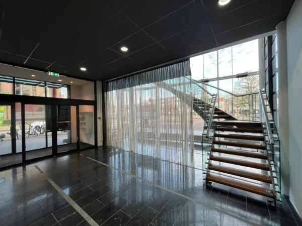 Moderne entreehal aan de Arnhemseweg met zwarte vloer, glazen trap en grote ramen met gordijnen.