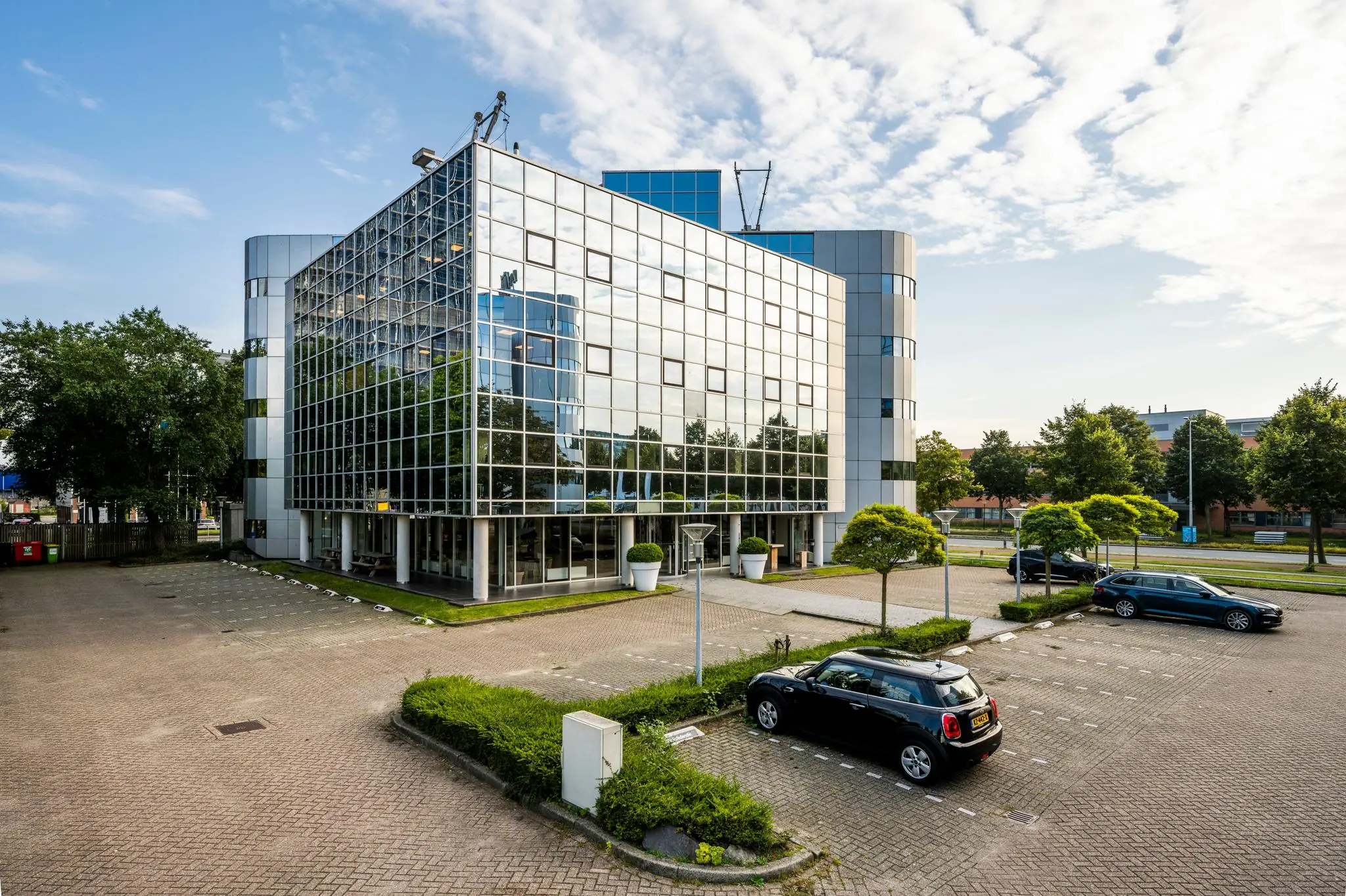 Modern kantoorgebouw aan de Hogehilweg met een glazen gevel en omliggende parkeerplaatsen.