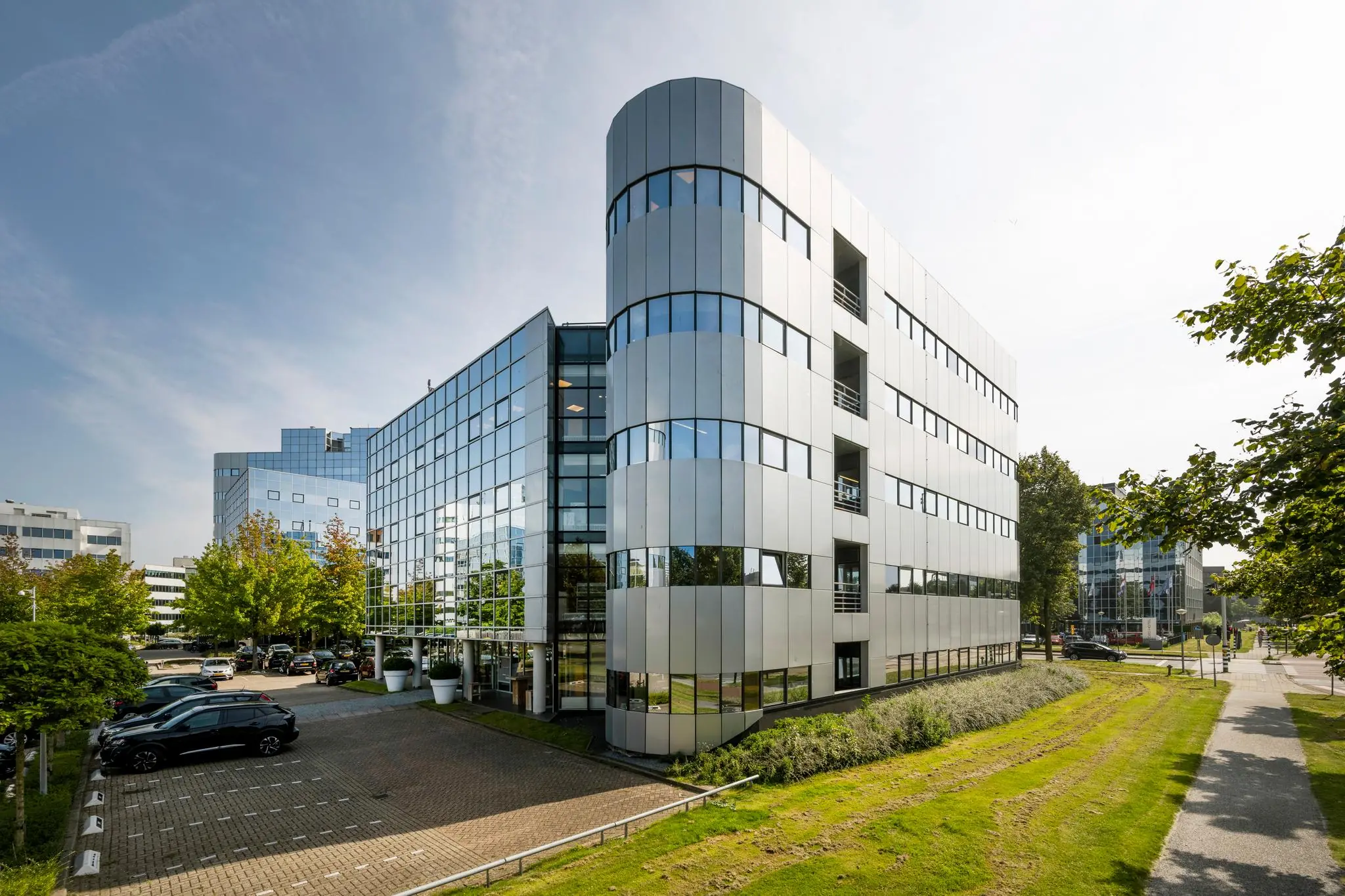 Modern kantoorgebouw aan de Hogehilweg in Amsterdam met glazen gevel en omliggende parkeerplaatsen.