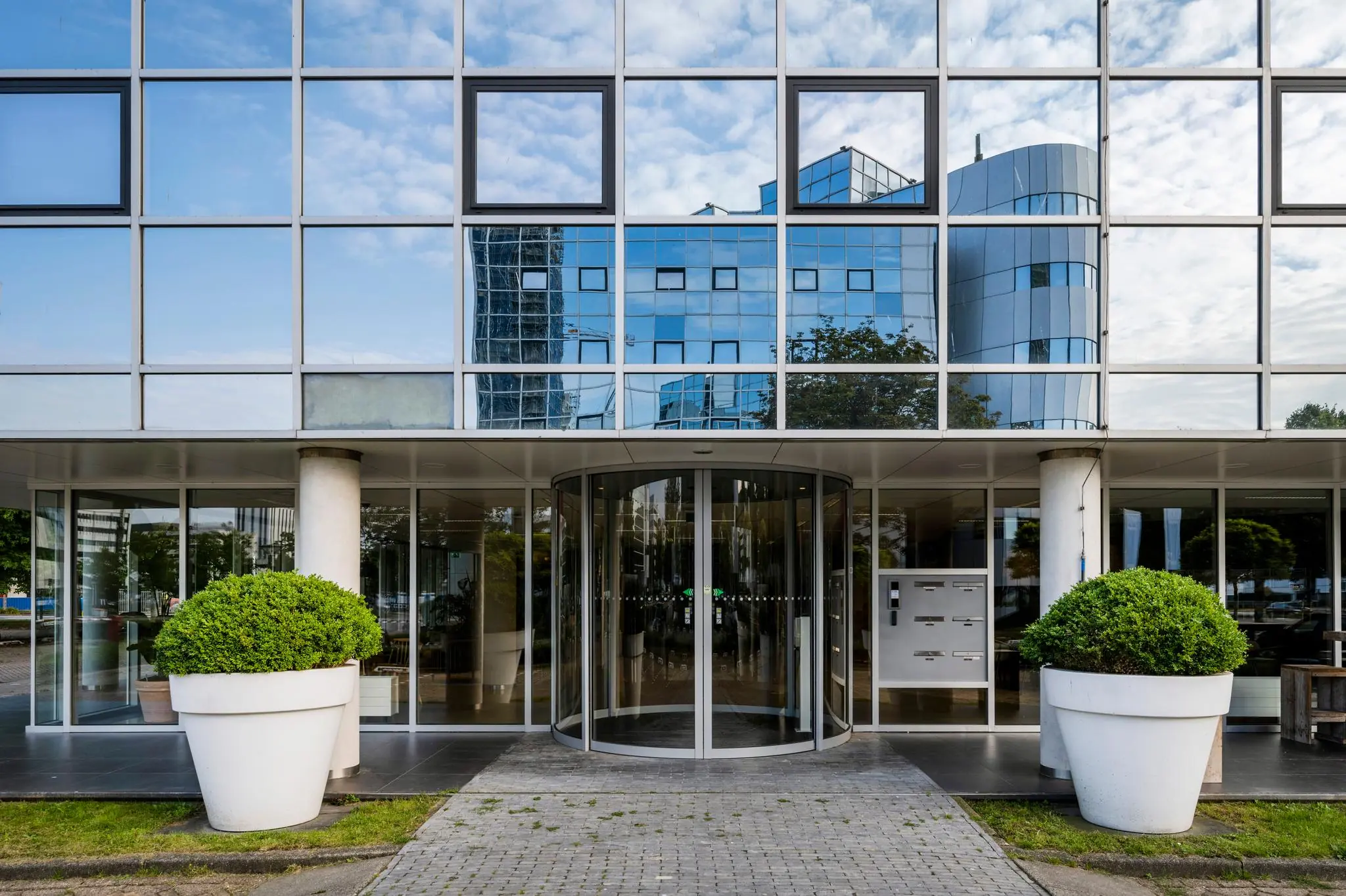 Ingang van een modern kantoorgebouw aan de Hogehilweg met glazen gevel en draaideur.