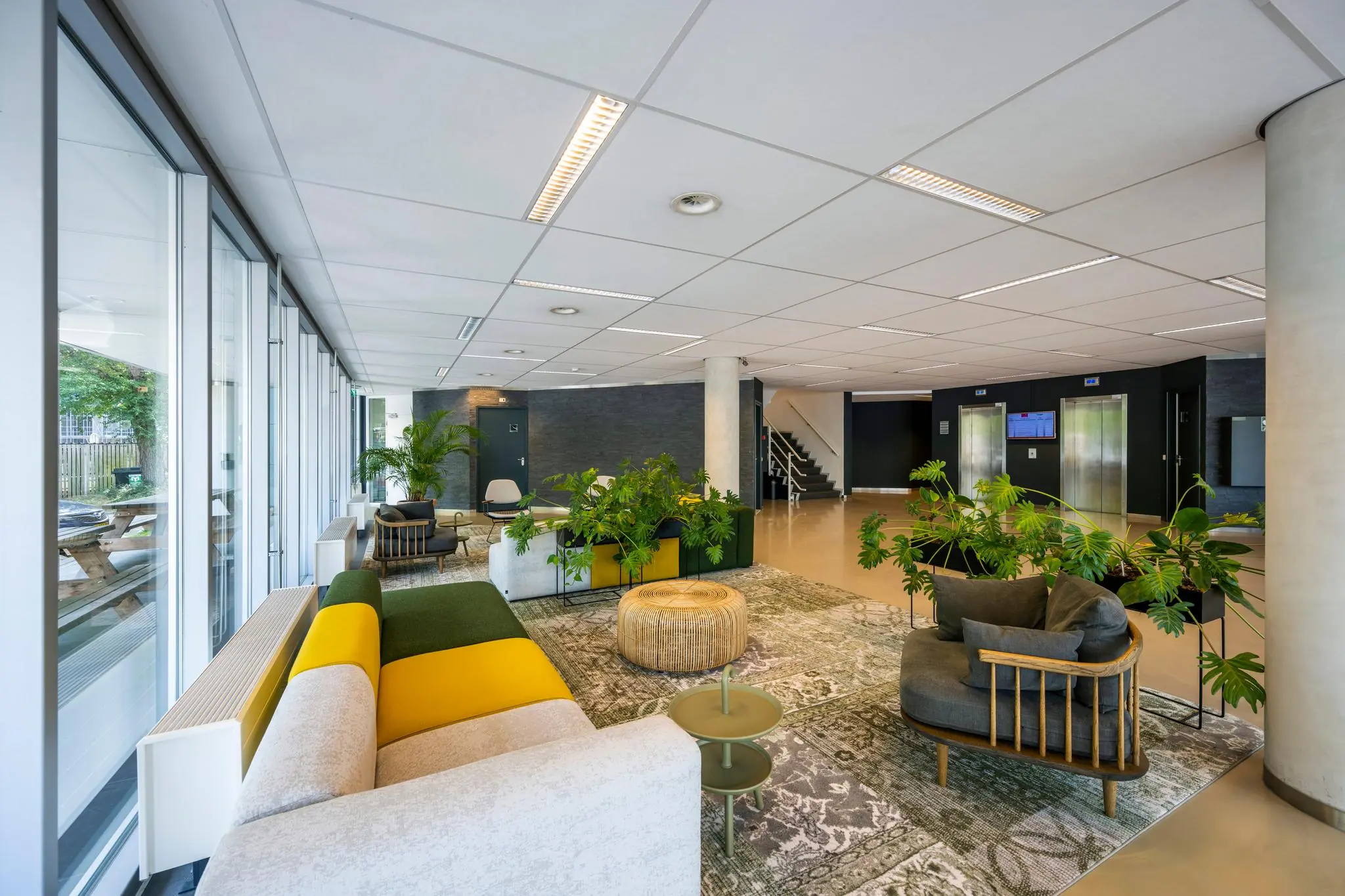 Moderne en kleurrijke lobby van een kantoorpand aan de Hogehilweg met zitgedeelte, planten en liften op de achtergrond.