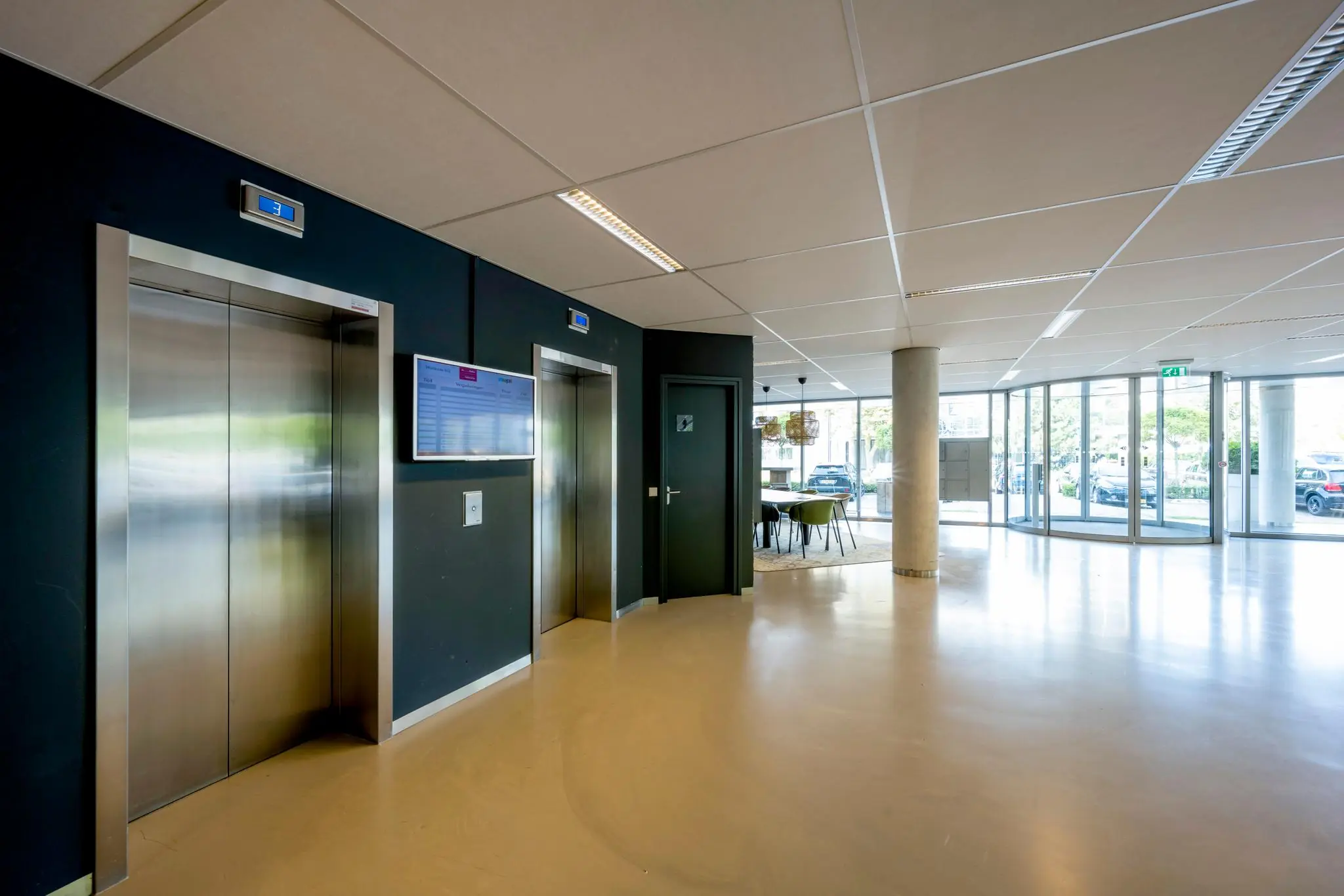 Moderne entreehal van een kantoorgebouw aan de Hogehilweg met liften, wachtruimte en glazen draaideur.