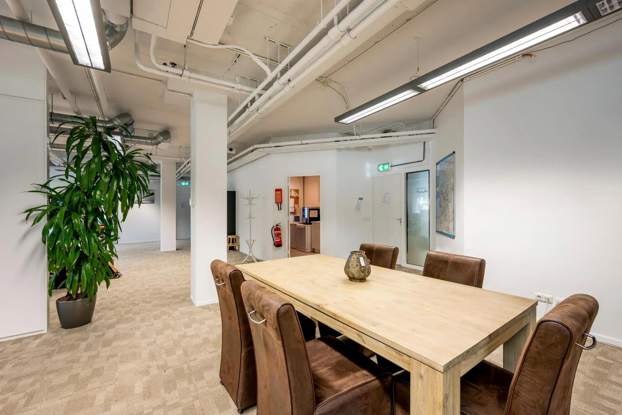 Vergaderruimte met houten tafel en zes bruine stoelen in kantoorpand aan de Hogehilweg.