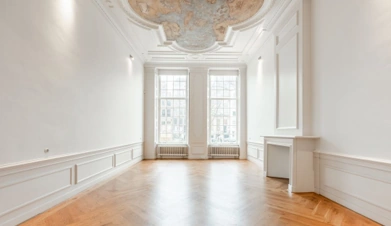 Licht en klassiek interieur aan de Keizersgracht met houten visgraatvloer, hoge ramen en plafondschildering.