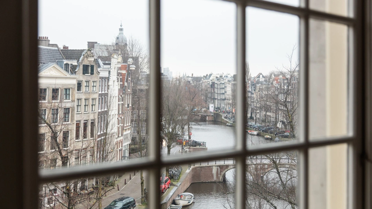 Uitzicht door een raam op de Keizersgracht in Amsterdam met grachtenpanden, brug en water.