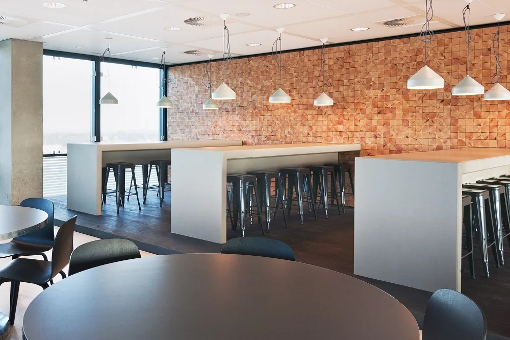 Moderne bedrijfskantine aan de Piet Heinkade met hoge tafels, barkrukken en een houten accentmuur.