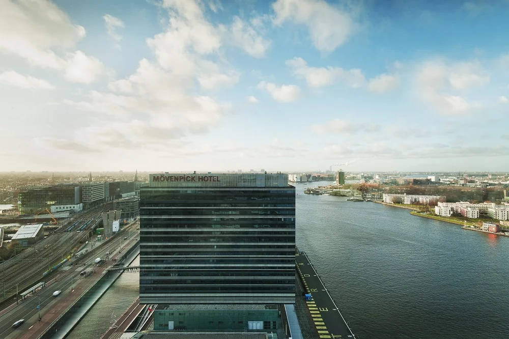 Luchtfoto van het Mövenpick Hotel aan de Piet Heinkade in Amsterdam, met zicht op het IJ en de omliggende stad.