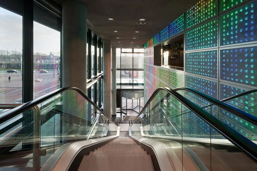Roltrap in modern gebouw aan de Piet Heinkade met kleurrijke LED-verlichte muurpanelen.