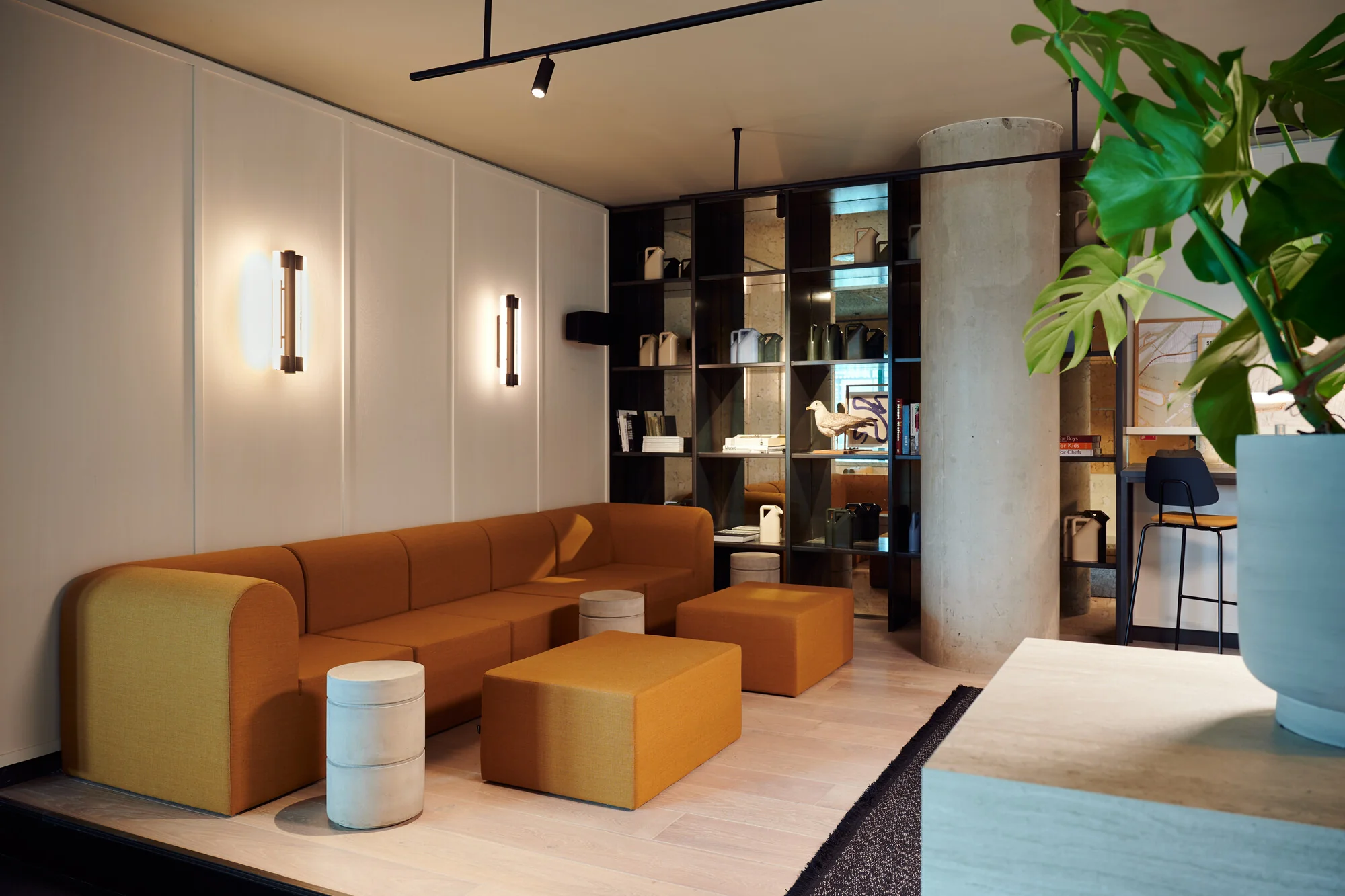 Moderne wachtruimte aan de Piet Heinkade met een oranje bank, designverlichting, open wandkast en grote kamerplant.
