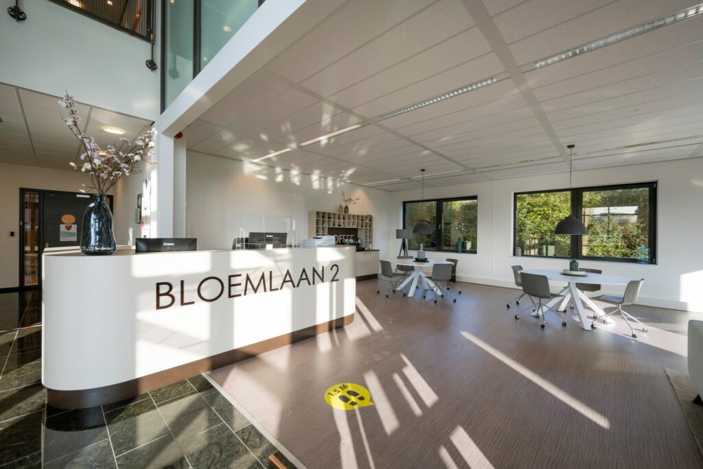 Moderne en lichte ontvangstruimte met een balie met opschrift "BLOEMLAAN 2", werkplekken en grote ramen.