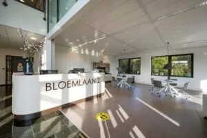 Moderne en lichte ontvangstruimte met een balie met opschrift "BLOEMLAAN 2", werkplekken en grote ramen.