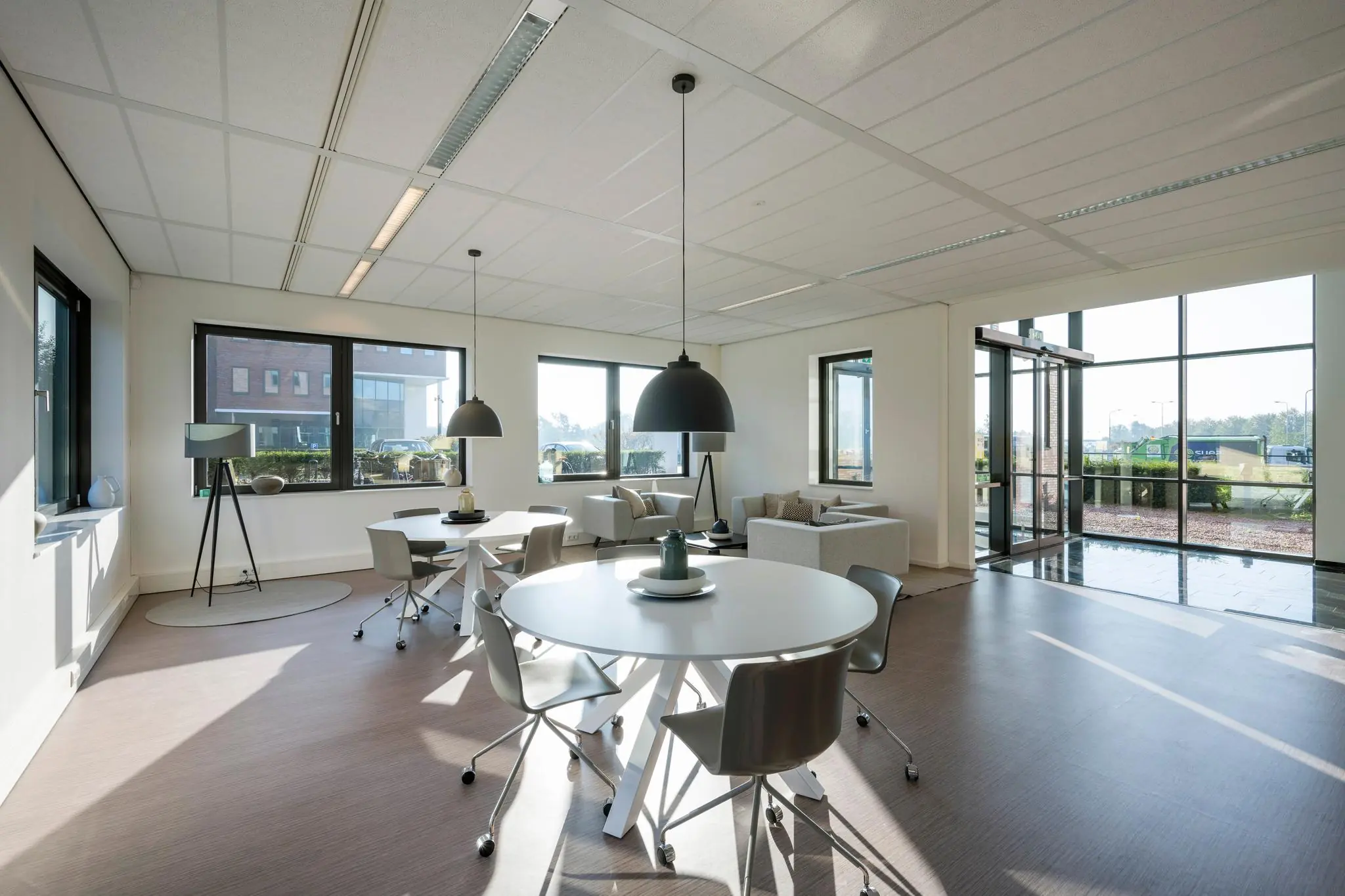 Moderne, lichte kantoorruimte aan de Bloemlaan met ronde vergadertafels, zithoeken en grote ramen.