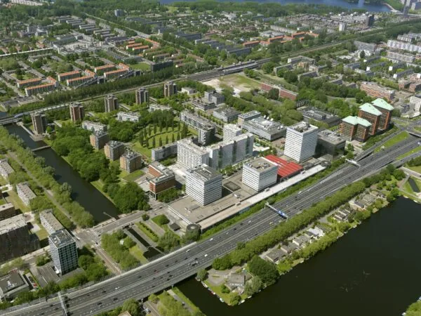 Luchtfoto van het Koningin Wilhelminaplein in Amsterdam met kantoren, woongebouwen, een snelweg en omliggend groen.