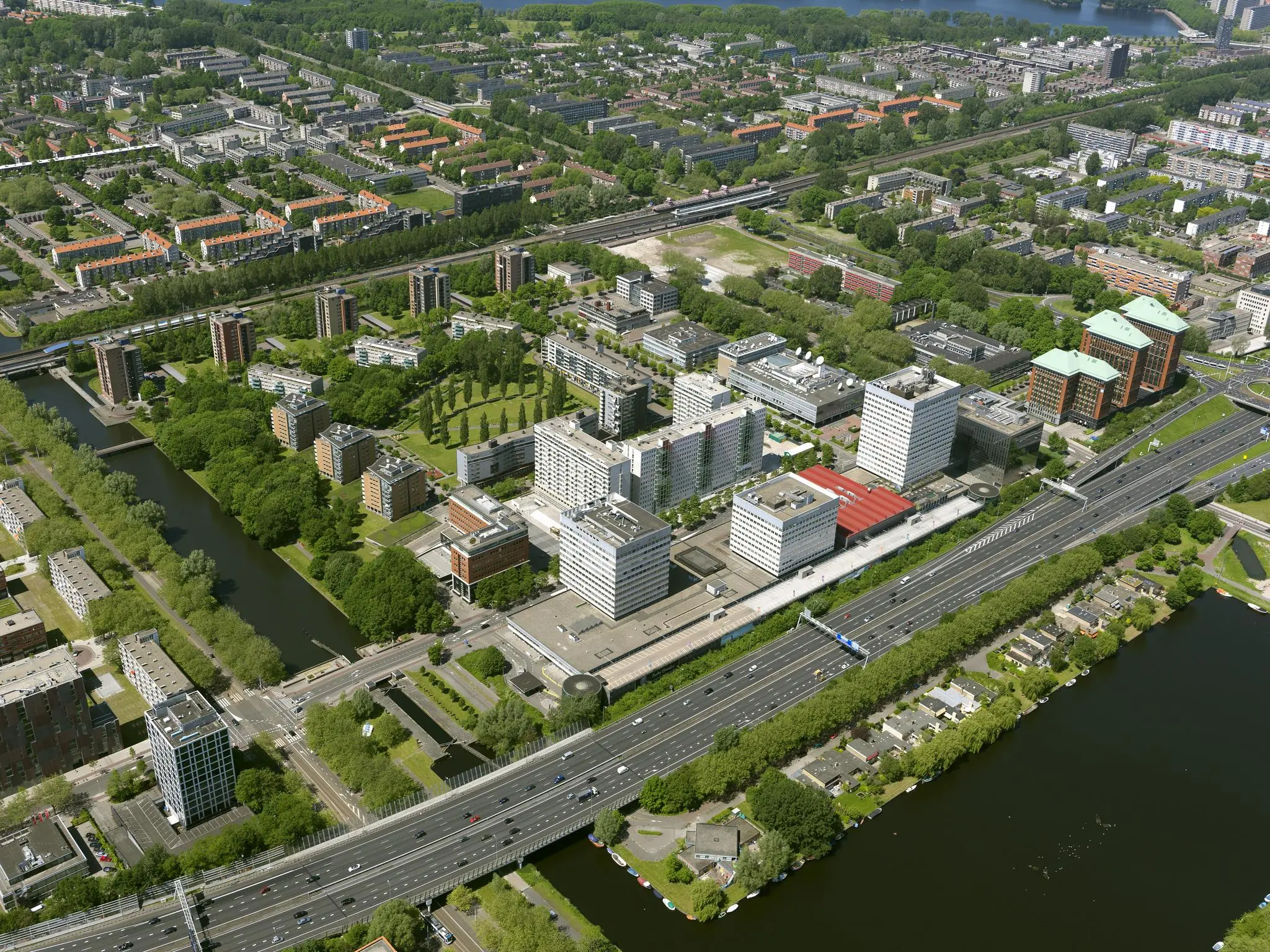 Luchtfoto van het Koningin Wilhelminaplein in Amsterdam met kantoren, woongebouwen, een snelweg en omliggend groen.