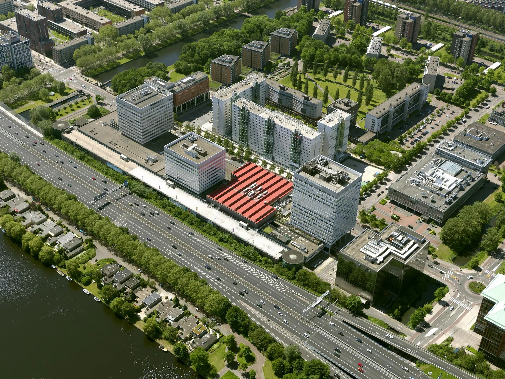 Luchtfoto van het Koningin Wilhelminaplein in Amsterdam met kantoorgebouwen, woonwijken en snelweg A10 op de voorgrond.