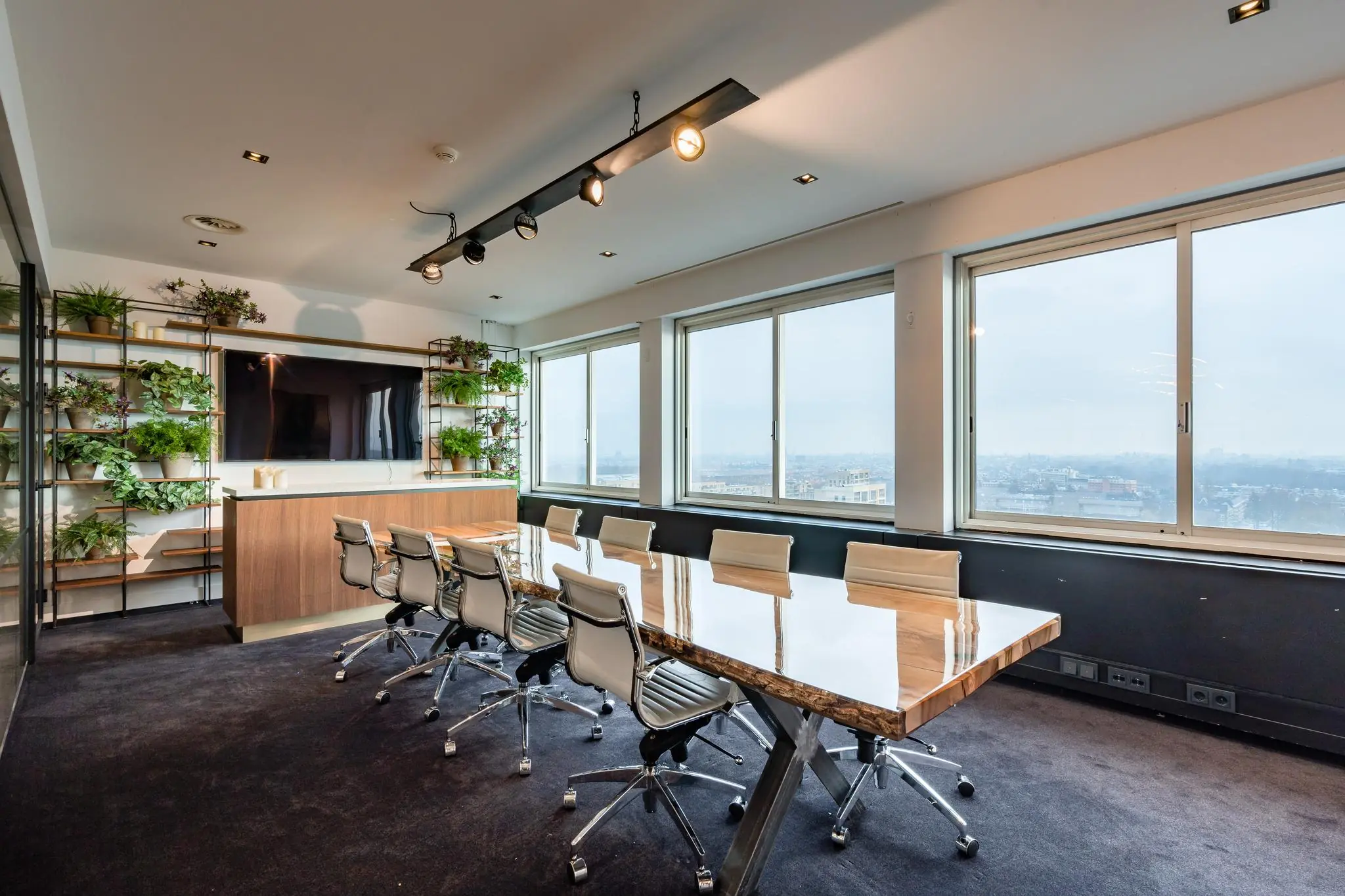 Moderne vergaderruimte met een lange houten tafel, designstoelen, een grote monitor en uitzicht over het Koningin Wilhelminaplein.