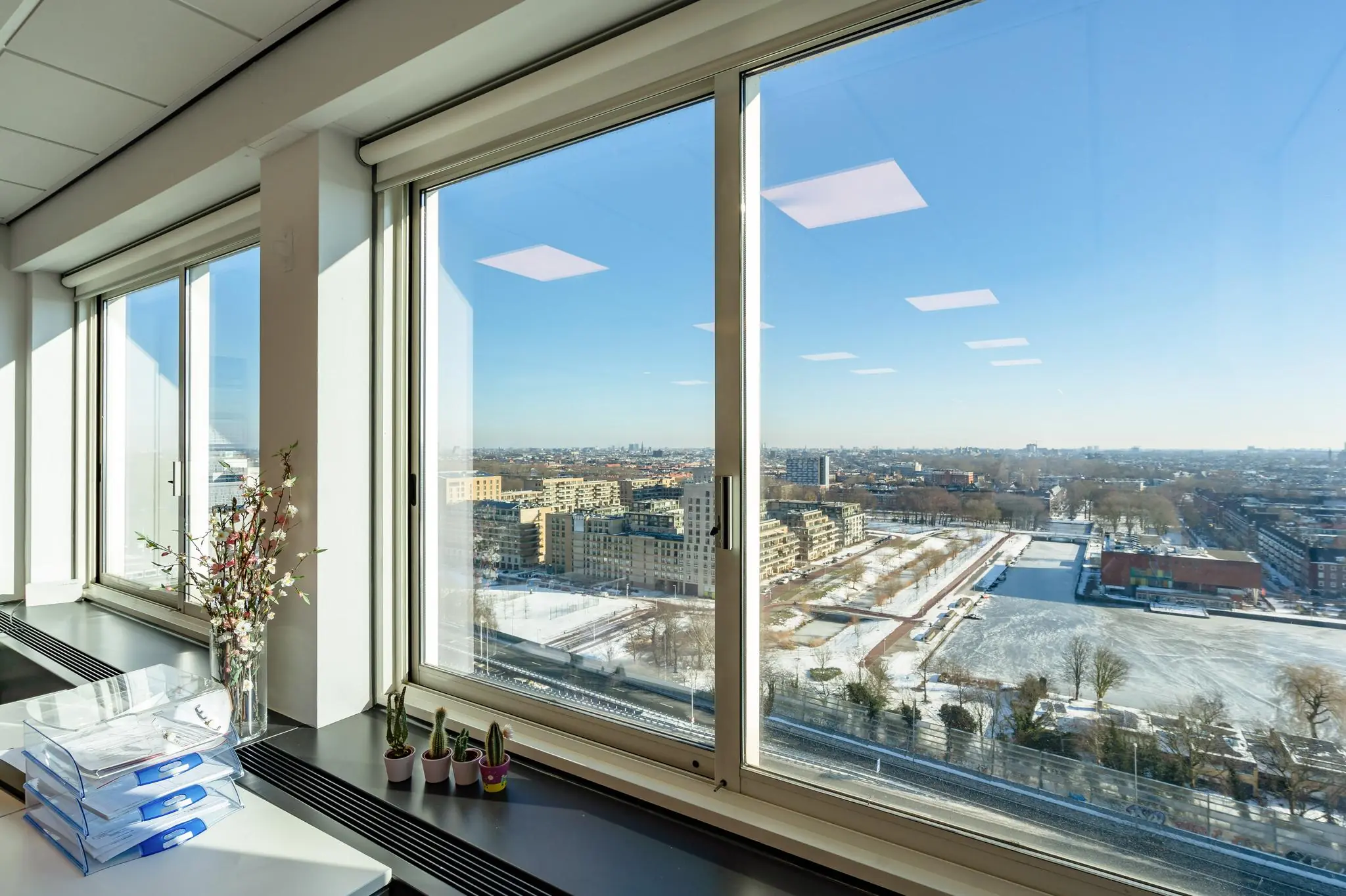 Uitzicht vanuit een modern kantoor op het besneeuwde Koningin Wilhelminaplein in Amsterdam.