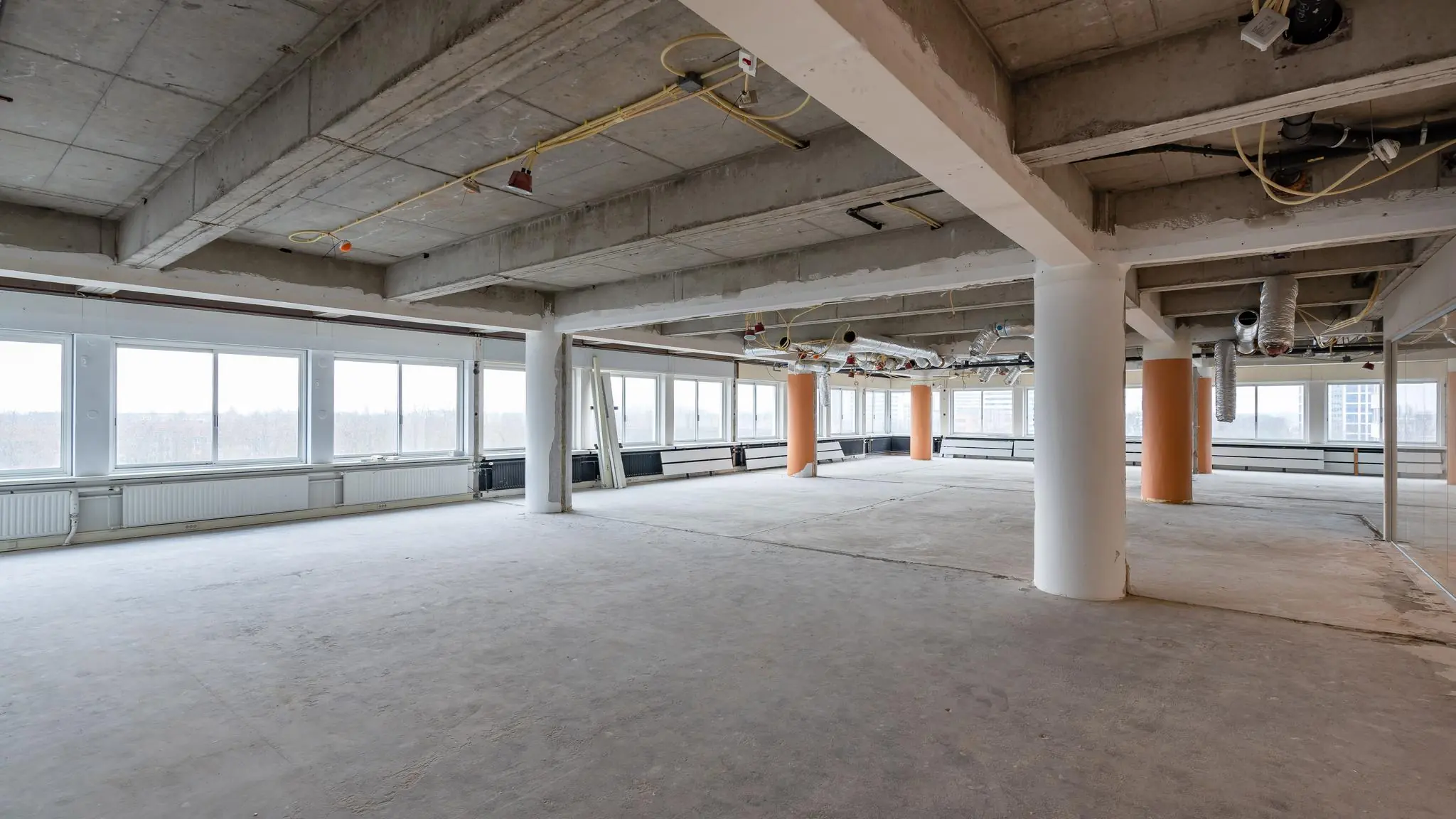 Leegstaand kantoorpand aan het Koningin Wilhelminaplein met zichtbare betonnen plafonds en onafgewerkte vloer.