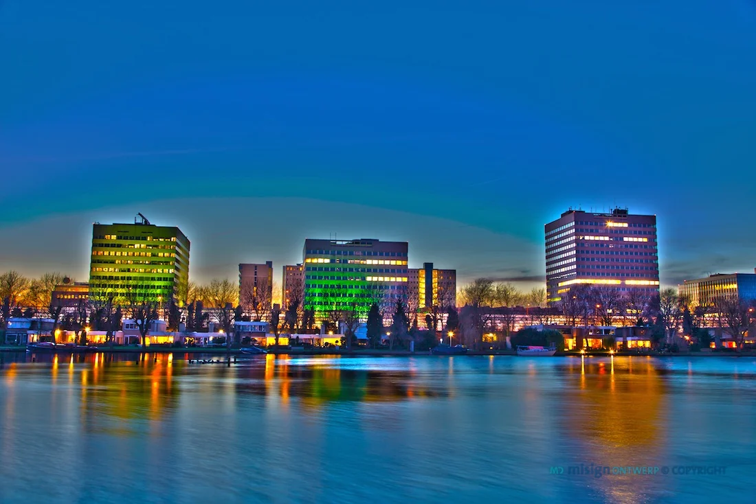 Skyline van het Koningin Wilhelminaplein in Amsterdam bij schemering, weerspiegeld in het water op de voorgrond.