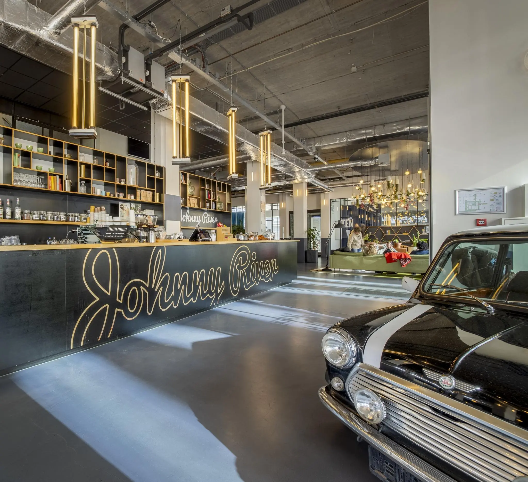 Moderne lobby met industriële inrichting, een balie met het logo "Johnny River", een zithoek en een klassieke zwarte Mini Cooper.