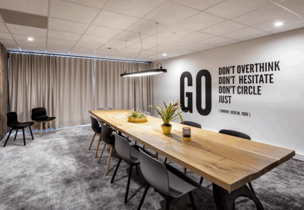 Moderne vergaderruimte aan de Joan Muyskenweg met een lange houten tafel, zwarte stoelen en inspirerende muurquote.