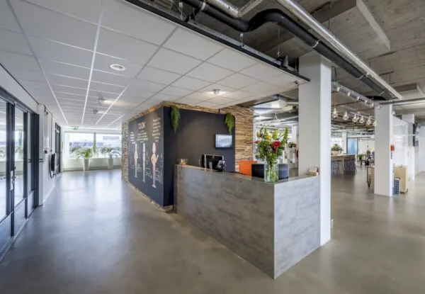 Moderne receptie met betonnen balie en kleurrijke bloemen bij TOON-kantoor aan de Joan Muyskenweg.