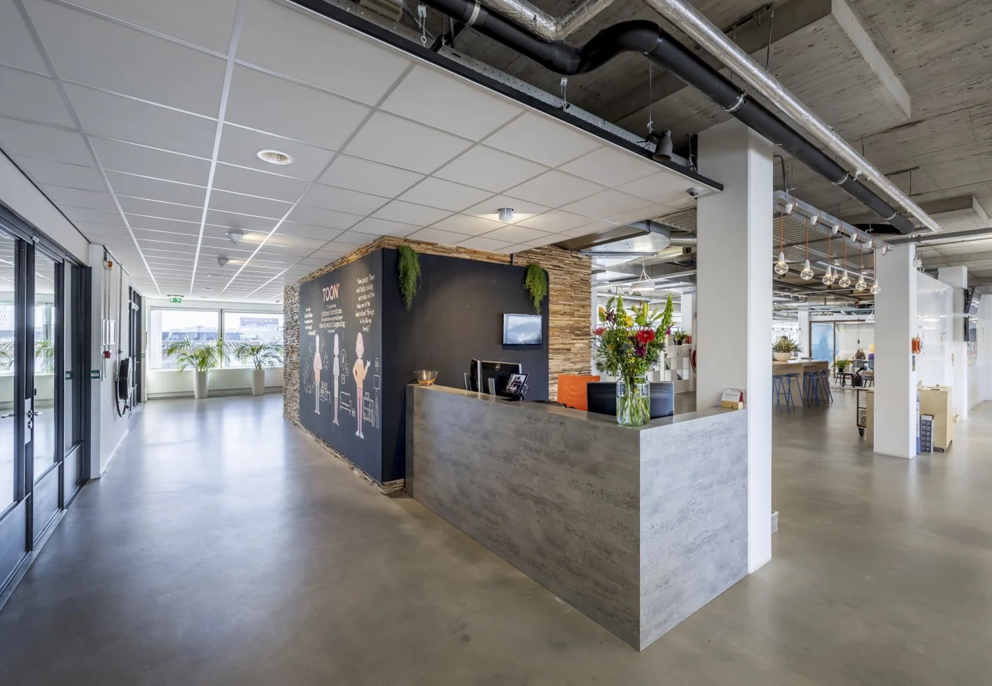Moderne receptie met betonnen balie en kleurrijke bloemen bij TOON-kantoor aan de Joan Muyskenweg.